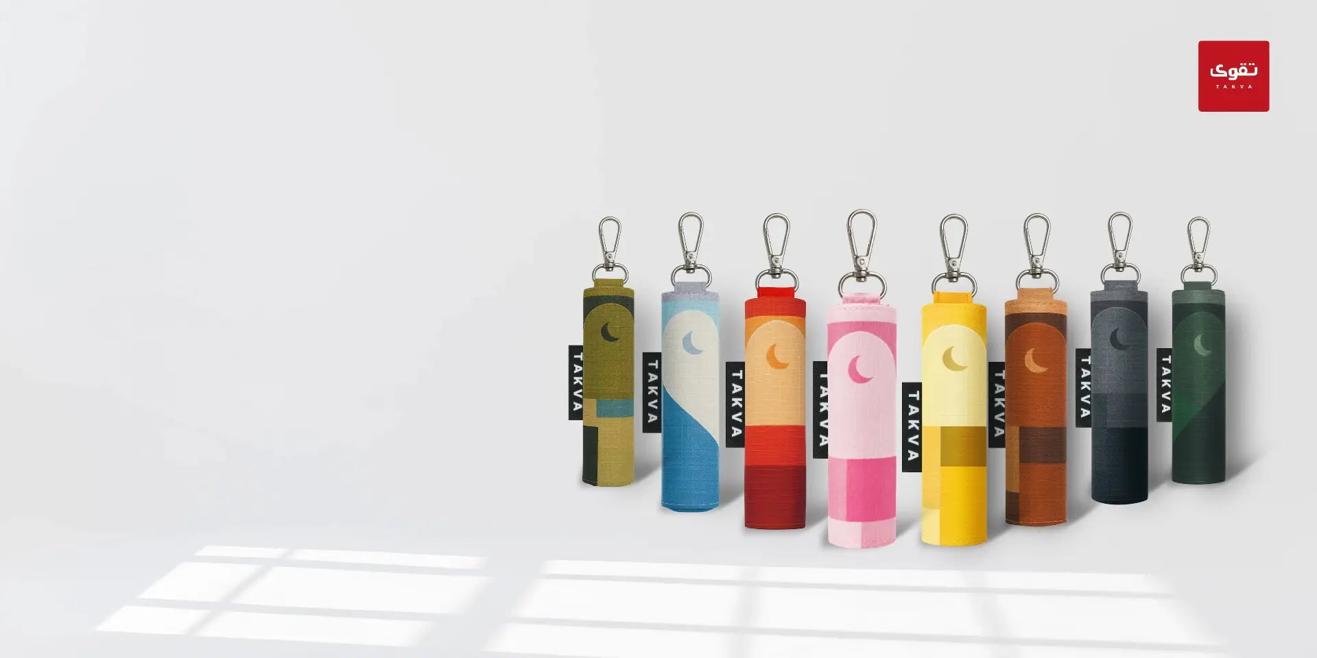 Seven colorful cylindrical keychain-prayer mats with different color block pattern, a crescent moon graphic and vertical black label reading 'TAKVA'.