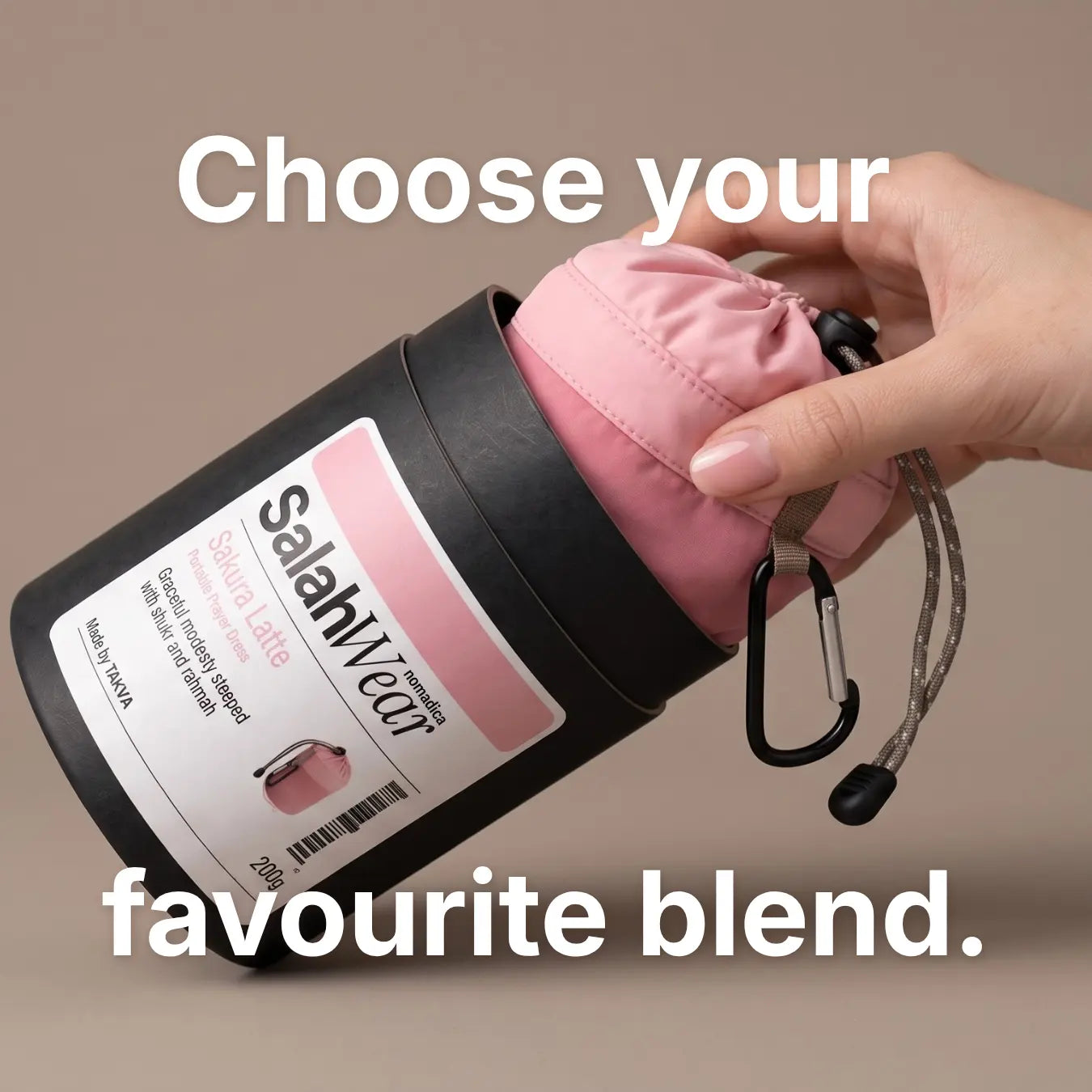 A hand pulls the pink Sakura Latte SalahWear travel prayer dress pouch out of its black kraft tube packaging, labelled 'SalahWear Nomadica: Sakura Latte, Portable Prayer Dress. Graceful modesty steeped with shukr and rahmah. Made by TAKVA, 200g. (Mobile Copy)