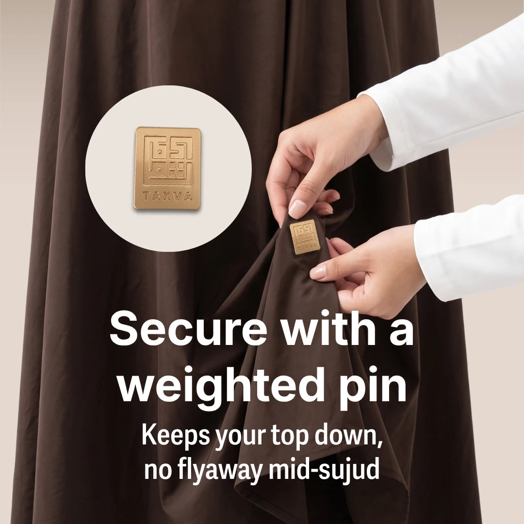  a close-up of the weighted pin that secures the top to the skirt so the mukena fabric doesn't fly up mid-sujud. Text overlay: 'Secure with a weighted pin — keeps your top down, no flyaway mid-sujud.' (Mobile Copy)